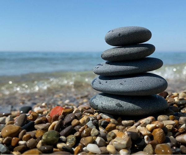 Balanced stones stacked on a peaceful beach with a calm sea in the background.